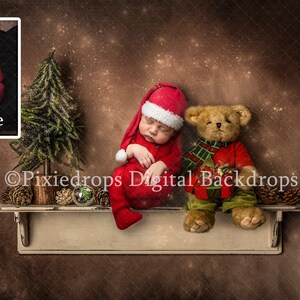 May include: A newborn baby wearing a red Santa hat and outfit, sleeping next to a teddy bear and a small Christmas tree. The scene is set on a shelf with pine cones and ornaments, against a brown backdrop with sparkling effects.