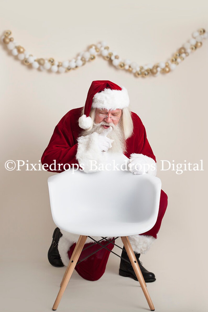 May include: Santa Claus in a red suit with white trim and a white beard is sitting on a white chair with wooden legs. He is looking down at the chair with a thoughtful expression.