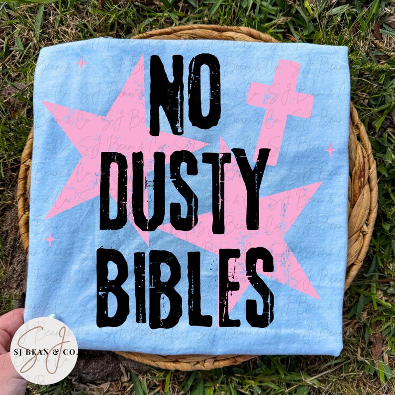 Peut inclure: Un t-shirt bleu clair avec le texte noir vieilli NO DUSTY BIBLES. Le motif comprend de grandes &eacute;toiles roses et un symbole de croix rose superpos&eacute;s derri&egrave;re le texte. Le t-shirt pr&eacute;sente un filigrane avec le texte SJ Bean & Co.