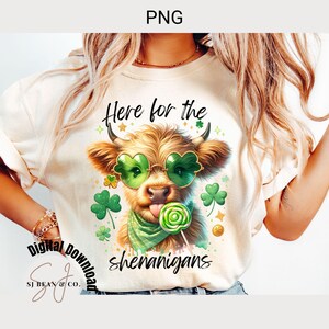 May include: A white t-shirt with a cartoon highland cow wearing green sunglasses and a green bandana. The cow is licking a green and white lollipop. The text "Here for the shenanigans" is printed on the shirt.