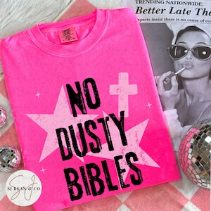 Peut inclure: Un t-shirt rose n&eacute;on vif arborant un grand motif d'&eacute;toile blanche et un symbole de croix blanche. Le texte NO DUSTY BIBLES est imprim&eacute; en lettres noires grasses et us&eacute;es au centre. Le t-shirt poss&egrave;de un col rond et une &eacute;tiquette de marque.