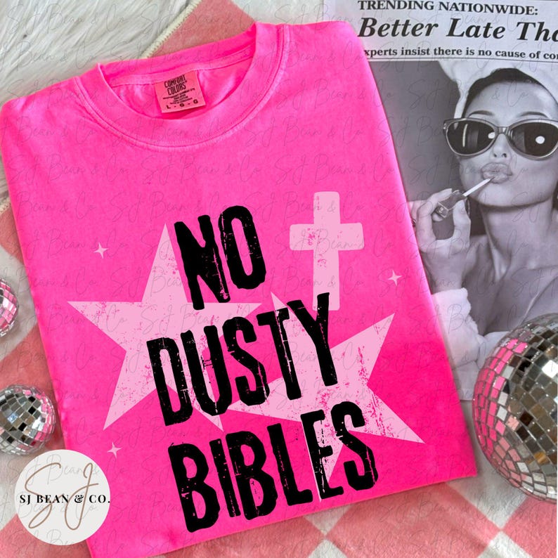 Peut inclure: Un t-shirt rose n&eacute;on vif arborant un grand motif d'&eacute;toile blanche et un symbole de croix blanche. Le texte NO DUSTY BIBLES est imprim&eacute; en lettres noires grasses et us&eacute;es au centre. Le t-shirt poss&egrave;de un col rond et une &eacute;tiquette de marque.
