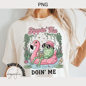 Sippin’ Tea Frog PNG design featuring a green frog in a pink bucket hat and sunglasses relaxing on a pink flamingo float, holding iced tea with lemon and umbrella. Surrounded by lily pads, plants, and “Do Not Disturb” sign. Perfect for sarcastic summer designs, vacation shirt sublimation, and quirky wall art.