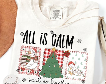 Könnte beinhalten: Cremefarbenes T-Shirt mit dem Text "ALL IS CALM said no teacher ever." Das Shirt zeigt drei gerahmte Illustrationen einer Ente mit Weihnachtsmütze, eines Weihnachtsbaums und einer Ente mit Lichterketten. Das Shirt hat ein Comfort Colors-Etikett.