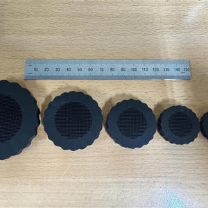 May include: Five black round speaker covers with a grid pattern in the center. The covers are different sizes and have a scalloped edge.