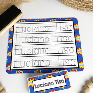 May include: A blue and yellow dry-erase board with a superhero theme. The board has four lines for writing practice. The name "Luciano Tiso" is written on the board. A separate wooden block with the same superhero theme and the name "Luciano Tiso" is also shown.