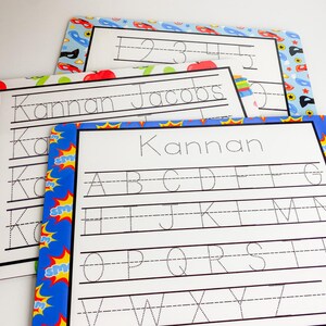 May include: Three dry-erase learning boards with colorful borders. The top board has numbers 1-5 written on it. The middle board has the name "Kannan Jacobs" written on it. The bottom board has the alphabet written on it.