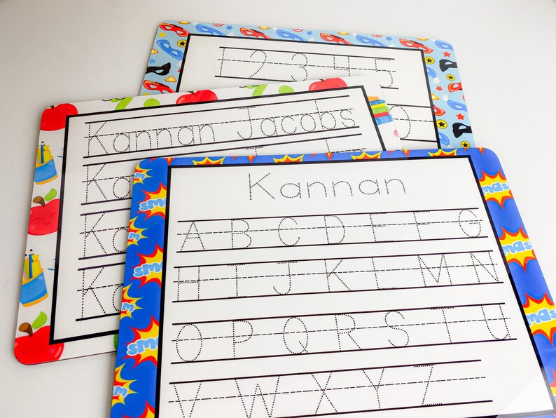 May include: Three dry-erase learning boards with colorful borders. The top board has numbers 1-5 written on it. The middle board has the name "Kannan Jacobs" written on it. The bottom board has the alphabet written on it.
