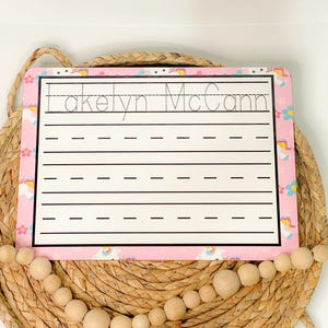 May include: Pink and white dry erase board with a unicorn theme. The board has a lined area for writing practice and the name "Jakelyn McCann" is written at the top.