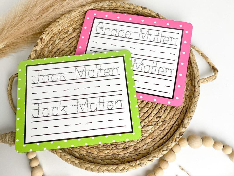 May include: Two green and pink dry-erase boards with white polka dots. The boards have dotted lines for practicing writing the names "Jack Mullen" and "Grace Mullen".