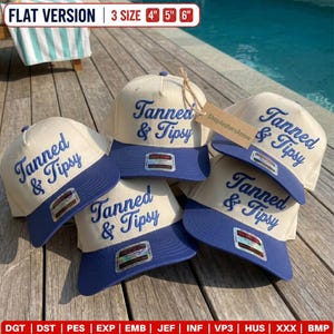 May include: Four beige baseball caps with blue brims, each featuring the embroidered blue text Tanned & Tipsy. The caps are available in 4 inch, 5 inch, and 6 inch sizes. A brown paper tag labeled ShopArchersArrow is attached to one cap.