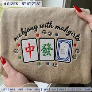 May include: Tan sweatshirt embroidered with the phrase "mahjong with mahgirls" in black script. Below the text are three embroidered Mahjong tiles with Chinese characters in red, green, and white. The sweatshirt is available in 4 sizes: 5", 6", 7", and 8".