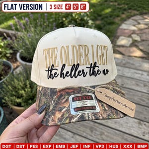 Op de afbeelding: Een crèmekleurige baseballpet met een klep in camouflagepatroon. De voorzijde is voorzien van geborduurde tekst in goud en zwart met de tekst "THE OLDER I GET the heller the no". Een rechthoekige sticker en een bruin papieren label zijn aan de klep bevestigd.
