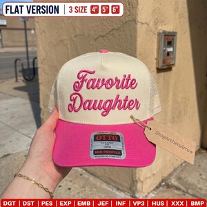 May include: A cream and hot pink trucker hat featuring the embroidered text Favorite Daughter in a cursive pink font. The hat includes a structured front panel, a mesh back, and a sticker on the brim that reads Otto Classic Fit Mid Profile.