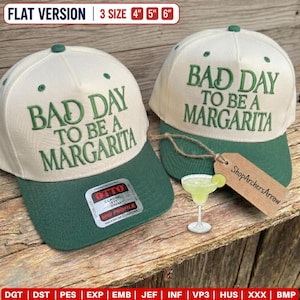 May include: Two cream-colored baseball caps with dark green brims and dark green embroidered text reading BAD DAY TO BE A MARGARITA. The caps feature a sticker on the brim and a brown tag attached by string. Text indicates 3 sizes: 4, 5, and 6 inches.