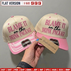May include: Two cream-colored baseball caps with pink brims and pink embroidered text that reads BLAME IT on the DRINK PACKAGE. Each cap features a silver Otto brand sticker on the brim and a brown cardboard tag attached by a string.