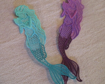 May include: Two mermaid-shaped lace appliques, one in shades of teal and turquoise, the other in shades of purple and lavender.