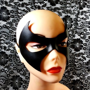 K&ouml;nnte beinhalten: Eine schwarze Ledermaske mit einem spitzen Design &uuml;ber den Augen. Die Maske wird auf einem Mannequin-Kopf getragen.