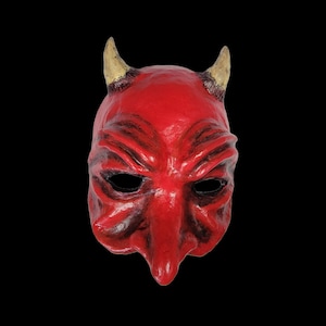 May include: Red devil mask with horns, made of paper mache. The mask has a detailed, textured face with a large, prominent nose.