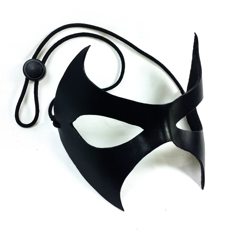 K&ouml;nnte beinhalten: Eine schwarze Leder-Maskenballmaske mit spitzem Design und einem schwarzen Gummiband.