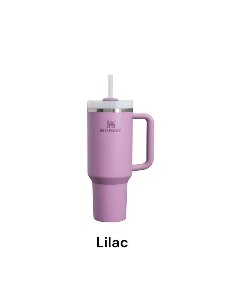 May include: A lilac-colored Stanley tumbler with a handle and a white lid and straw. The Stanley logo is visible on the side. The word "Lilac" is written in a black font at the bottom of the image.