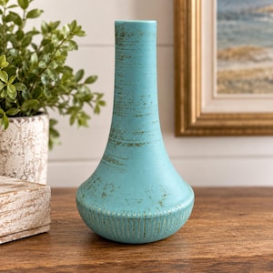 May include: A turquoise vase with a narrow neck and a wide, rounded base. The surface features a distressed, textured finish with horizontal brush strokes and vertical ribbing along the bottom edge of the vessel.