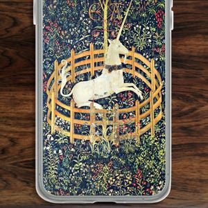 May include: A phone case featuring a detailed tapestry design. The artwork depicts a white unicorn within a wooden fence, surrounded by a floral and foliage background in shades of blue, green, and red. The case has a clear border.