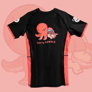 May include: Black and coral rash guard with a cartoon octopus and person graphic. The text "LET'S TANGLE" is printed below the graphic. The shirt has coral accents on the sides and sleeves.