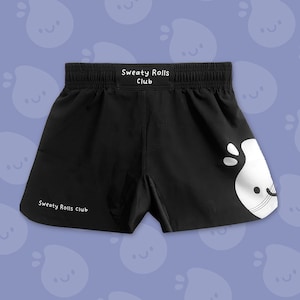 Peut inclure: Short de sport noir avec l'inscription "Sweaty Rolls Club" imprimée en blanc. Un dessin blanc d'un personnage souriant est sur la jambe droite. Le short a une taille élastique.