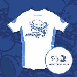 以下が含まれることがあります： 白地に青いアクセントと漫画のグラフィックが特徴のスポーツTシャツ。グラフィックは、笑顔のキャラクターと青いドラゴンを描き、「KISS OF THE DRAGON」の文字が入っています。シャツには「SWEATY ROLLS CLUB」の文字も入っています。