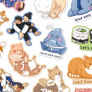Peut inclure: Une collection d'autocollants découpés présentant des illustrations de dessins animés, dont deux personnes en tenue d'arts martiaux blanche et noire, une goutte bleue avec une ceinture blanche marquée white belt tears, des sushis et des chats.