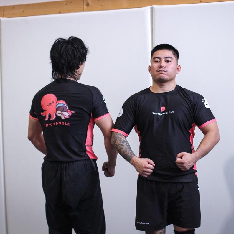 May include: Black athletic shirts with pink accents and matching shorts. The shirts feature a cartoon octopus graphic with the text "LET'S TANGLE" on the back and "Sweaty Rolls Club" on the front.