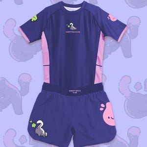 May include: A navy blue athletic set featuring a short-sleeved top and matching shorts. The top has pink accents and the text "SWEATY ROLLS CLUB". The shorts also have the text "SWEATY ROLLS CLUB". Both pieces have cartoon graphics.