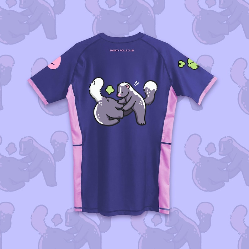 May include: A navy blue athletic shirt with pink accents and a cartoon skunk graphic. The shirt features the text "SWEATY ROLLS CLUB" on the back. The sleeves and sides have pink trim, and a pink circle and green shapes are on the sleeves.