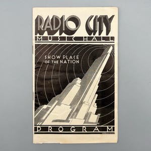 Könnte beinhalten: Ein Vintage-Programmcover der Radio City Music Hall. Das Cover zeigt die Worte "Radio City Music Hall" in einem kühnen Art-Deco-Stil mit dem Satz "Show Place of the Nation" darunter. Das Programm ist ein Schwarz-Weiß-Design.