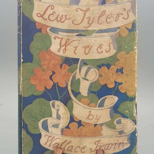 Puede incluir: Una cubierta de libro vintage con fondo azul y diseño floral. El título es "Lew Tyler's Wives" de Wallace Irwin.