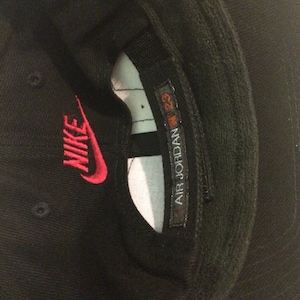 May include: Black baseball cap with a red Nike logo and a white label that says "AIR JORDAN 23"