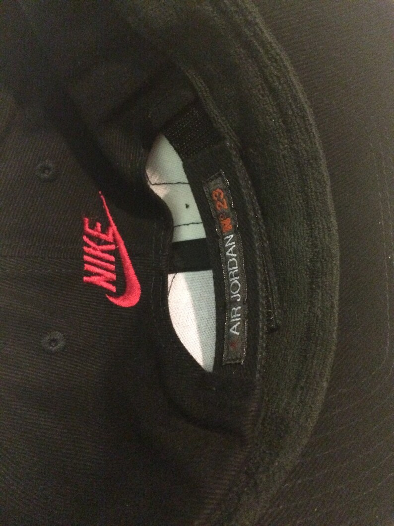 May include: Black baseball cap with a red Nike logo and a white label that says "AIR JORDAN 23"