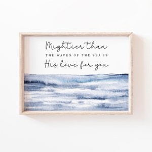 May include: A framed print featuring a watercolour painting of blue ocean waves. The text "Mightier than the waves of the sea is His love for you" is printed in black on a white background.