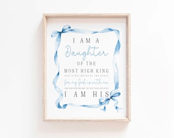 May include: A framed wall art print featuring a light blue watercolour ribbon border surrounding the text: I AM A Daughter OF THE MOST HIGH KING WHO IS NOT MOVED BY THE WORLD for my God is with me AND GOES BEFORE ME I DO NOT FEAR BECAUSE I AM HIS.