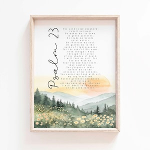 May include: A framed print featuring Psalm 23 in elegant script. The artwork showcases a watercolor landscape with mountains, trees, and wildflowers in shades of green, yellow, and orange. The frame is a light wood color.