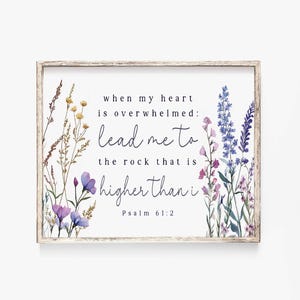 以下が含まれることがあります： フレームに入ったプリントで、花のイラストと「when my heart is overwhelmed: lead me to the rock that is higher than i Psalm 61:2」のテキストが特徴です。 アートワークには、紫、青、黄色の花が含まれています。
