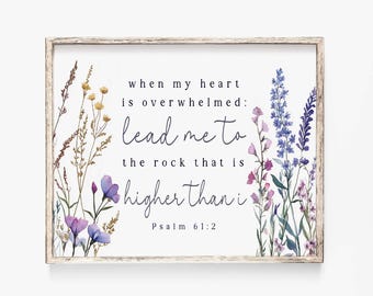 May include: A framed print with floral artwork and the text "when my heart is overwhelmed: lead me to the rock that is higher than i Psalm 61:2". The artwork features purple, blue, and yellow flowers, with a light wooden frame.