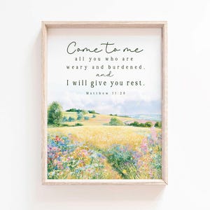 May include: A framed wall art print featuring a landscape painting of a golden wheat field and colorful wildflowers under a cloudy sky. The text reads: Come to me all you who are weary and burdened, and I will give you rest. Matthew 11:28.