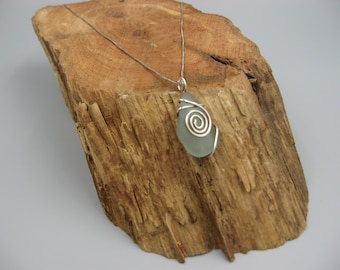 May include: A silver chain necklace with a light blue sea glass pendant wrapped in silver wire. The pendant has a spiral design.