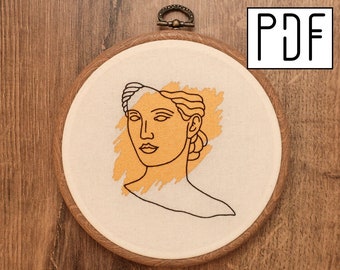 Pode incluir: Um bastidor de bordado circular de madeira contendo tecido branco sujo com um retrato de linha preta de um busto clássico sobreposto a uma pincelada texturizada amarelo mostarda. O topo do bastidor apresenta um fecho metálico e o texto PDF.