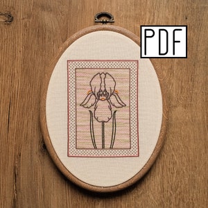 May include: An oval wooden embroidery hoop containing a fabric panel with a stitched iris flower design. The iris is outlined in dark thread with orange accents, set against a background of horizontal pink and green stripes and a dotted border. PDF text.
