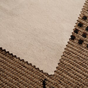 May include: A close-up of a beige fabric with a slightly textured surface. The fabric is folded over and the edge is slightly scalloped.