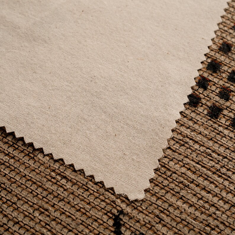 May include: A close-up of a beige fabric with a slightly textured surface. The fabric is folded over and the edge is slightly scalloped.