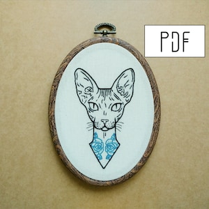 May include: Embroidered design of a Sphynx cat with blue roses on its chest, framed in a wooden oval hoop.